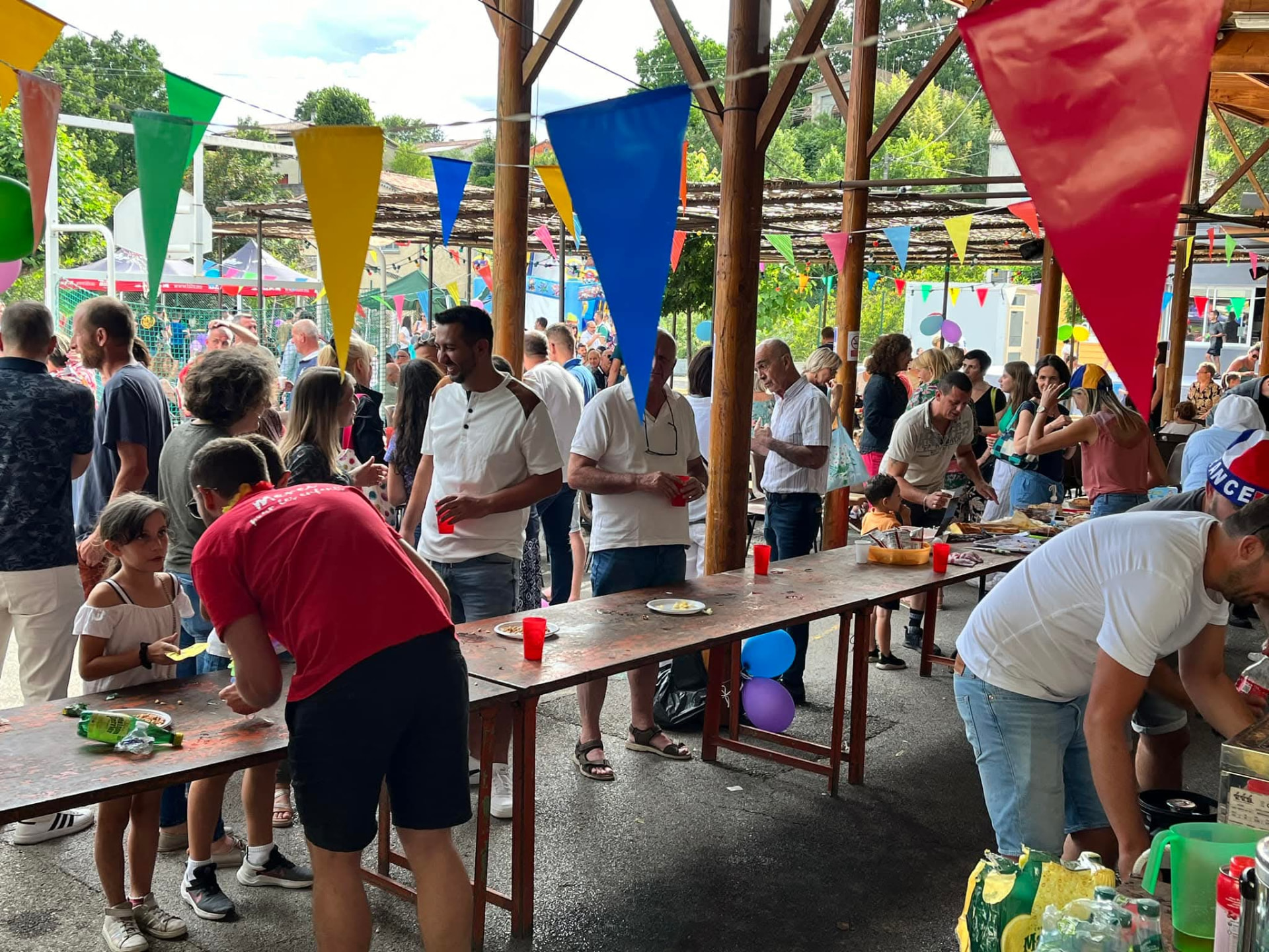 La fête de l'amicale sous le préau : longues tables, fanions colorés et familles réunies